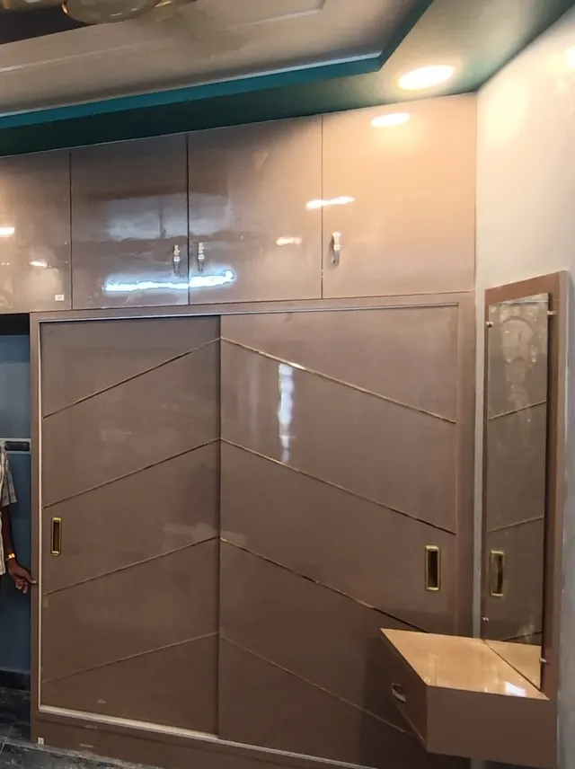 Sliding wardrobe in taupe gloss with brass inlay lines, overhead lofts and a dressing mirror