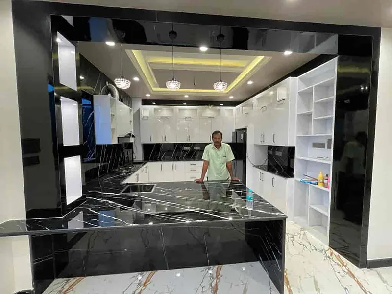Modular kitchen with a black marble-finish island, white cabinets and a cove-lit ceiling