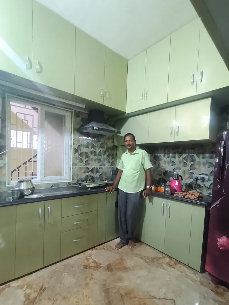 A completed sage green modular kitchen with a member of the Deepak Interiors team standing in front
